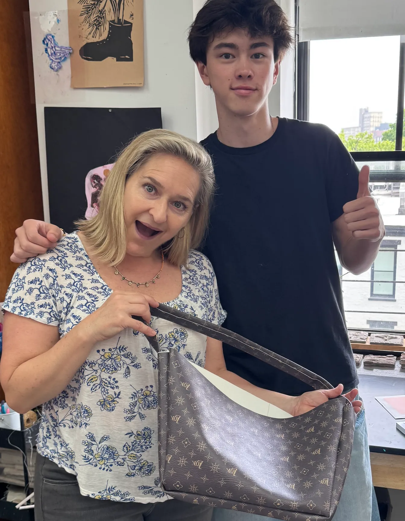 Dr. Nell Daniel holds up a brown monogram-patterned handbag while a student gives a thumbs up.
