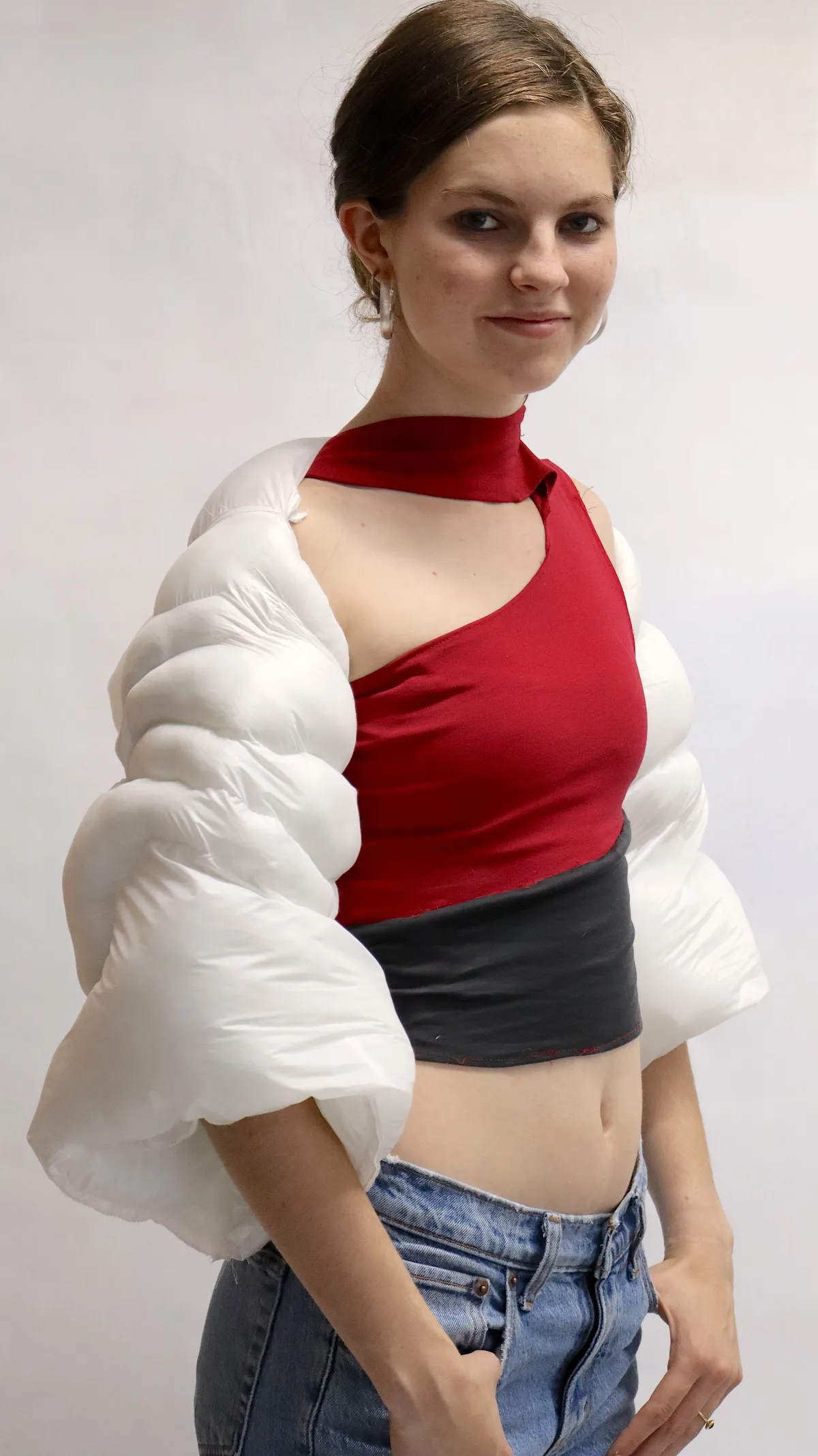 Model in a studio wears a white quilted bolero over a red asymmetric top and jeans.