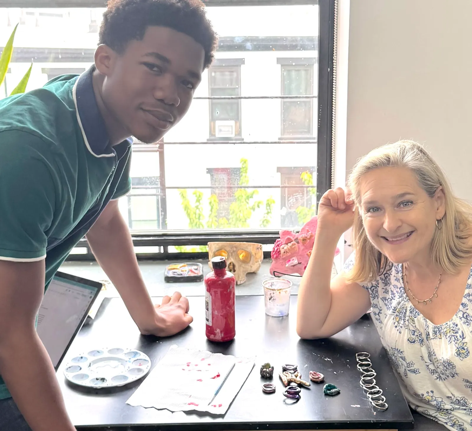 Dr. Nell Daniel and a student lean over a worktable of painted enamel jewelry pieces.
